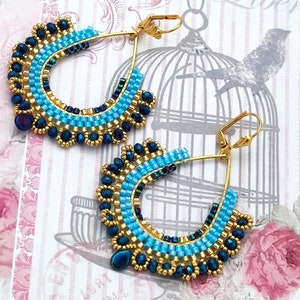 May include: A pair of gold hoop earrings with blue and black beads. The earrings are teardrop shaped and have a beaded fringe.