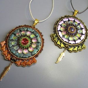 May include: Two beaded necklaces with dreamcatcher pendants. The pendants are round and feature a colorful mandala design with iridescent beads. One pendant is green and turquoise, the other is purple and pink. Both pendants have a gold feather charm.