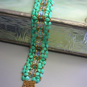 Könnte beinhalten: Ein türkisfarbenes und goldenes Armband mit einem Verschluss. Das Armband besteht aus kleinen, runden Perlen und hat ein geometrisches Muster.