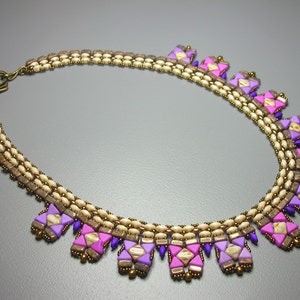May include: A multi-strand necklace with a geometric design. The necklace is made with beige, pink, and purple beads and features a brass clasp.