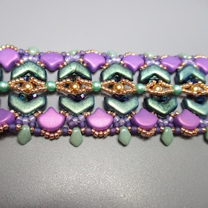 Könnte beinhalten: Nahaufnahme eines Armbands mit Perlen in einem geometrischen Muster. Das Armband besteht aus lila, grünen und goldenen Perlen.