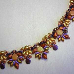 May include: A close-up of a beaded necklace with a geometric pattern. The necklace is made with purple, brown, and gold beads.