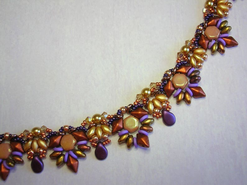 May include: A close-up of a beaded necklace with a geometric pattern. The necklace is made with purple, brown, and gold beads.