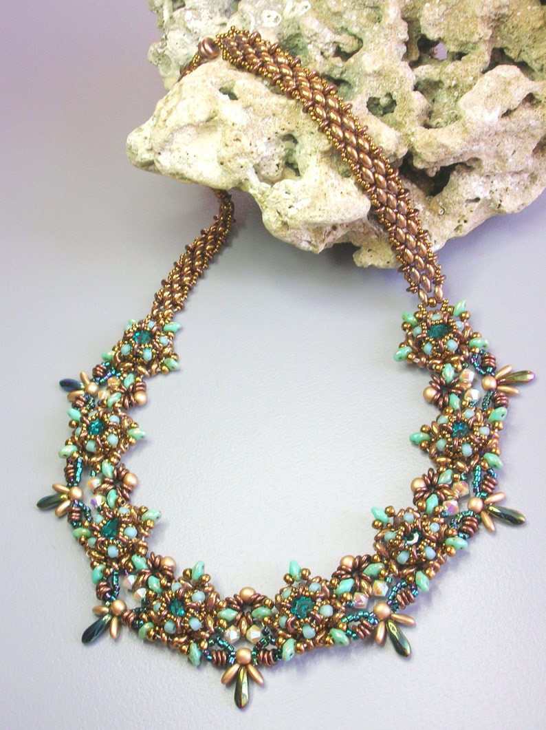 May include: A copper and green beaded necklace with a floral design. The necklace is made with small, round beads and features a repeating pattern of flowers.