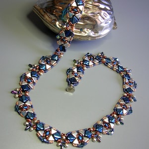 May include: A silver and blue beaded necklace with a matching bracelet. The necklace is made of small, faceted beads in shades of blue, silver, and copper. The bracelet is a shorter version of the necklace, with the same bead pattern.