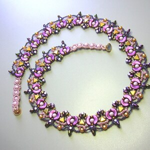 Op de afbeelding: Een paarse en gouden kralenketting met een bloemenmotief. De ketting is gemaakt van kleine, ronde kralen en heeft een delicate, vrouwelijke uitstraling.