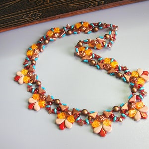 Könnte beinhalten: Halskette mit floralem Design aus Perlen. Die Kette hat eine Mischung aus Farben, darunter Rot, Orange, Braun und Türkis. Die Halskette besteht aus kleinen Perlen und hat ein zartes Aussehen.