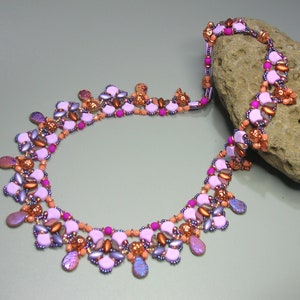 May include: A multi-strand necklace with pink, purple, and copper beads. The necklace is made with a variety of different shapes and sizes of beads, and it has a delicate and feminine look.