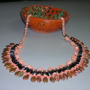 Może przedstawiać: Delikatny naszyjnik z kaskadowym wzorem z miedzianych koralików w kształcie liści, czarnych i tęczowych koralików oraz różowych koralików.
