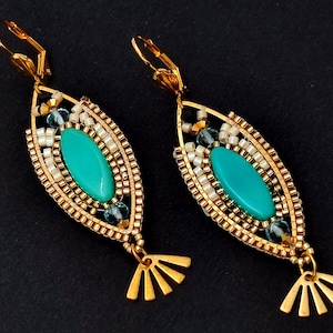 May include: A pair of gold earrings with a teal oval-shaped stone surrounded by gold and white beads. The earrings have a fan-shaped dangle.