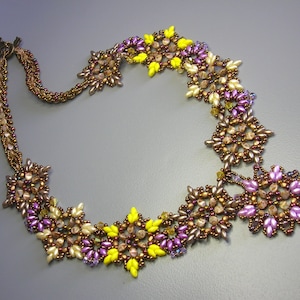 Op de afbeelding: Een kralenketting met een bloemenpatroon. De ketting is gemaakt van bruine, paarse en gele kralen. De ketting is ongeveer 45 centimeter lang.