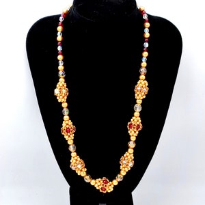 Könnte beinhalten: Eine goldene Perlenkette mit roten und klaren Kristall-Akzenten. Die Kette hat ein sich wiederholendes Muster aus goldenen Perlen und Kristall-Akzenten.