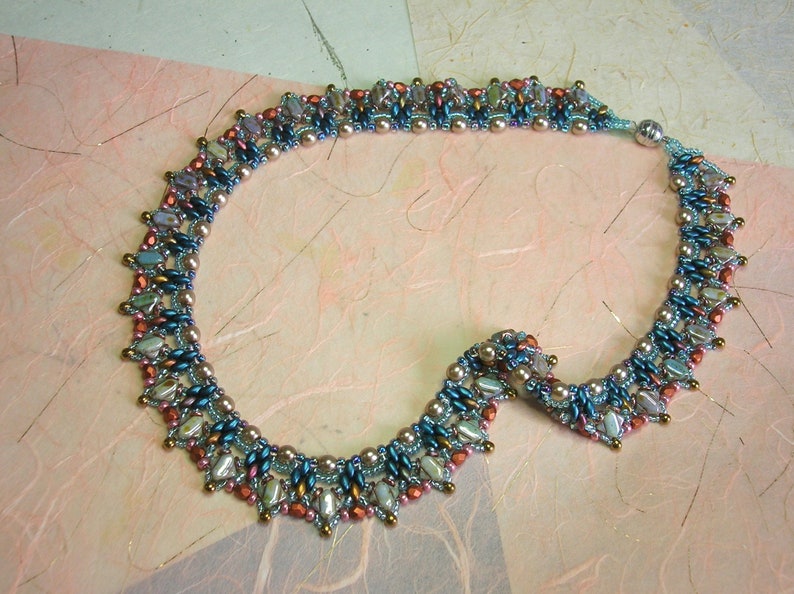 Puede incluir: Un collar de cuentas con un dise&ntilde;o graduado que presenta cuentas azules, marrones y rosas. El collar est&aacute; hecho con cuentas de diferentes tama&ntilde;os y tiene un aspecto delicado y femenino.