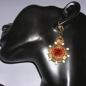 Op de afbeelding: Gouden en witte kralen oorbellen met een bruin middelste deel. De oorbellen hangen aan het oor van een mannequin.