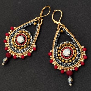 May include: Pair of teardrop-shaped earrings with gold-tone metal frames. The earrings feature intricate beadwork in red, gold, black, and white. A red bead and a faceted bead dangle from the bottom of each earring.