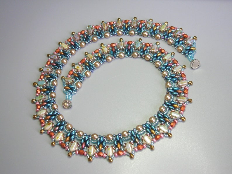 Puede incluir: Un collar de cuentas de m&uacute;ltiples hilos con un patr&oacute;n geom&eacute;trico en tonos de turquesa, melocot&oacute;n y dorado. El collar est&aacute; hecho con cuentas peque&ntilde;as y redondas y tiene un cierre magn&eacute;tico.