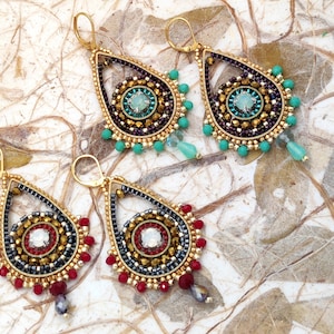 Puede incluir: Pendientes dorados en forma de lágrima con intrincados abalorios en turquesa, rojo, dorado y negro. Los pendientes presentan una piedra central y cuentas colgantes. El diseño es ornamentado y llamativo, perfecto para añadir un toque de elegancia.