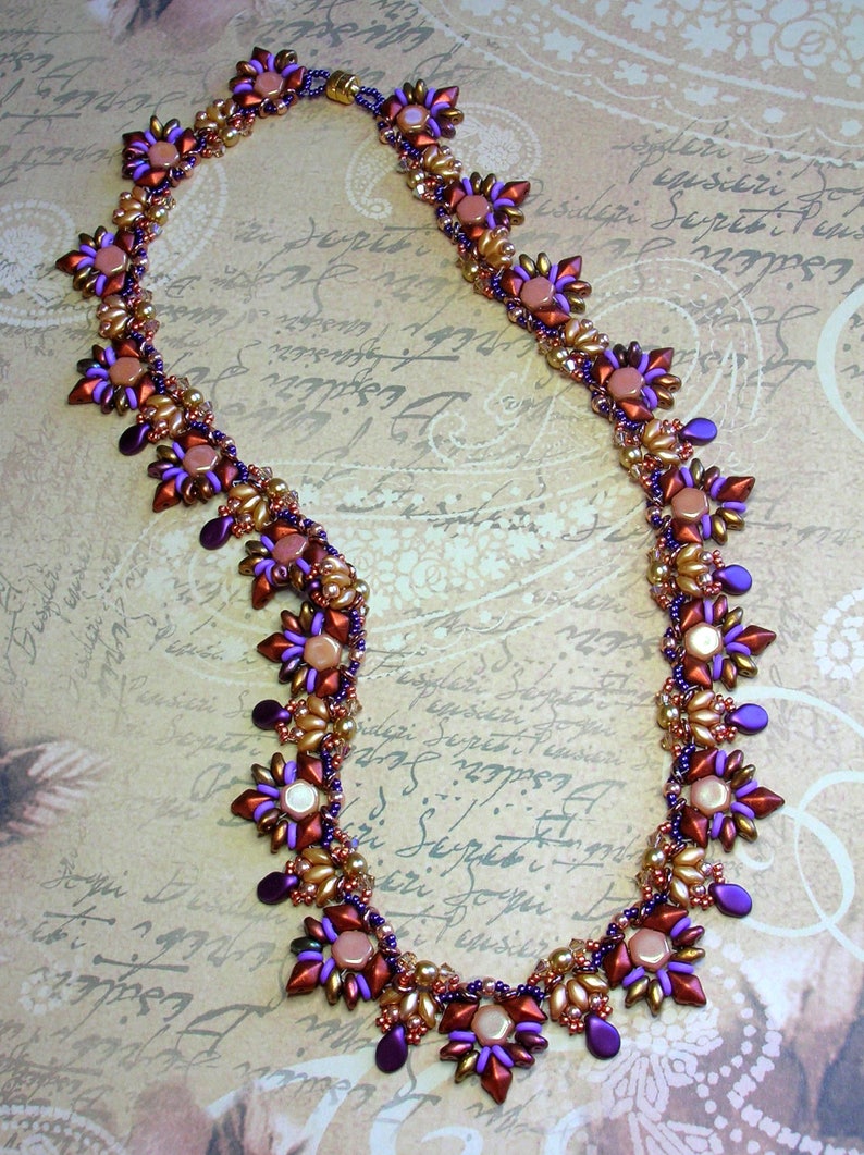 May include: A beaded necklace with a geometric design featuring purple, brown, and gold beads. The necklace is made with small, faceted beads and has a delicate, intricate design.