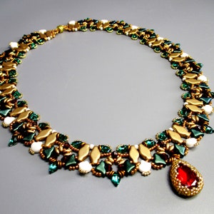 May include: A gold, green and white beaded necklace with a red teardrop pendant. The necklace is made with small, faceted beads and has a delicate, intricate design.