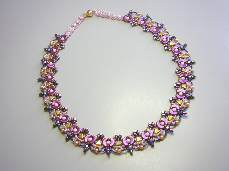 Op de afbeelding: Een delicate ketting gemaakt met paarse, roze en gouden kralen in een bloemmotief.