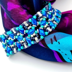 May include: A blue and turquoise beaded bracelet with silver accents. The bracelet is wrapped around a colorful patterned fabric.