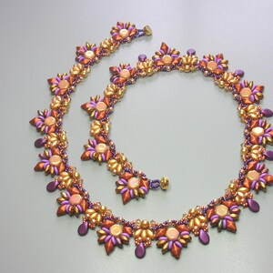 May include: A beaded necklace with a floral design in shades of purple, gold, and orange. The necklace is made of small, round beads and has a delicate, feminine look.