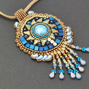 May include: A beaded necklace with a large, round pendant featuring a blue and gold sunburst design. The pendant has a blue gemstone in the centre and is surrounded by gold beads and blue and gold teardrop-shaped beads.