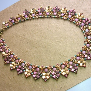 Op de afbeelding: Een delicate kralenketting met een gouden, roze en groene kleurstelling. De ketting is gemaakt van kleine, gefacetteerde kralen die in een geometrisch patroon zijn gerangschikt.