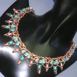 Può includere: Una collana di perline in rame e turchese con un design delicato e intricato. La collana presenta una varietà di perline, tra cui piccole perline rotonde, perline ovali più grandi e perline a forma di goccia. La collana è accentuata da un filo di rame e ha un design pendente.