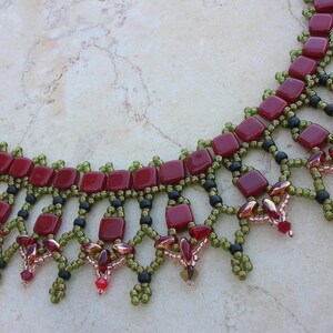 Peut inclure: Un collier de perles rouge et vert avec un motif géométrique. Le collier est fait de petites perles carrées et a une frange de perles plus petites.