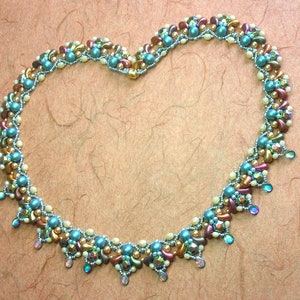 May include: A heart-shaped beaded necklace with a variety of colors, including teal, brown, gold, and white. The necklace is made with small, round beads and has a delicate, feminine look.