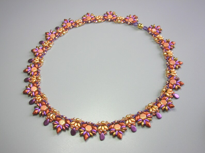 May include: A beaded necklace with a gold and purple color scheme. The necklace is made of small, round beads arranged in a floral pattern.