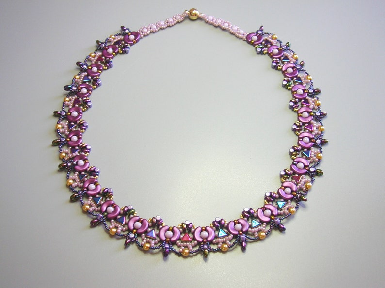 Op de afbeelding: Een delicate kralenketting met een bloemenmotief. De ketting is gemaakt van roze, paarse en gouden kralen.