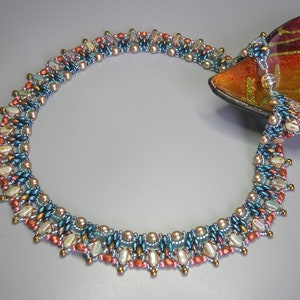 Puede incluir: Un collar de cuentas multicadena con un dise&ntilde;o graduado. El collar presenta una variedad de colores, incluyendo azul verdoso, cobre y crema. Las cuentas est&aacute;n dispuestas en un patr&oacute;n geom&eacute;trico, creando un aspecto &uacute;nico y llamativo.