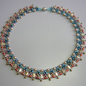 Puede incluir: Un collar de cuentas de m&uacute;ltiples hilos con una mezcla de cuentas azules, marrones y blancas. El collar tiene un borde festoneado decorativo.