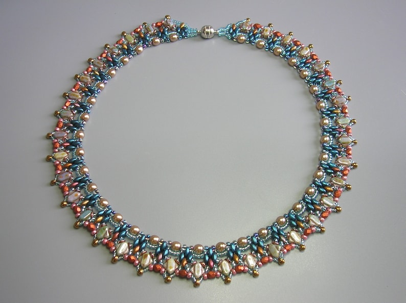 Puede incluir: Un collar de cuentas de m&uacute;ltiples hilos con una mezcla de cuentas azules, marrones y blancas. El collar tiene un borde festoneado decorativo.