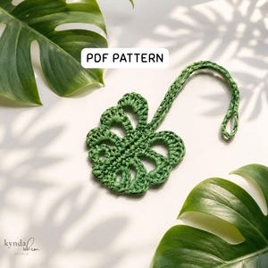 May include: A dark green crochet monstera leaf ornament with a hanging loop. The text PDF PATTERN is displayed in a white rectangular box above the leaf. The design features open cutouts characteristic of a monstera leaf shape.