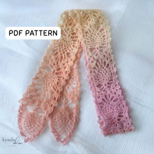 May include: A handmade, ombre crochet bookmark in shades of peach and pink. The bookmark features an openwork floral design and is finished with small pearl beads. The text "PDF PATTERN" is displayed in a white box. The Kynda Whim Studio logo is in the bottom left corner.