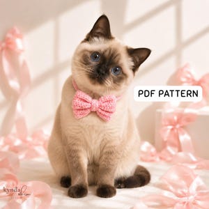May include: A Siamese cat with blue eyes wearing a light pink crocheted bow tie collar. The cat has dark brown fur on its ears, face, and tail, with light tan fur on its body. A white rectangular sign with black text reads PDF PATTERN.