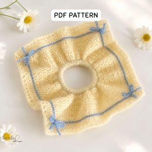 Pode incluir: Uma scrunchie de cabelo de malha amarelo claro com uma borda e laços azuis claros. A scrunchie tem uma abertura circular no centro. O texto "PDF PATTERN" está no topo. A marca "kynda whim studio" está no canto inferior esquerdo.