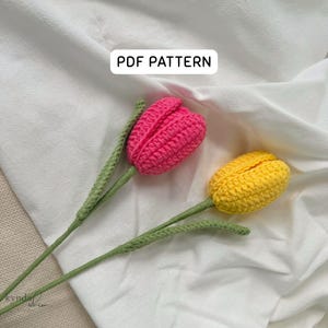 May include: Two crocheted tulip flowers, one pink and one yellow, with green stems and leaves. The flowers are set against a white background. The text "PDF PATTERN" is in a white rectangle.