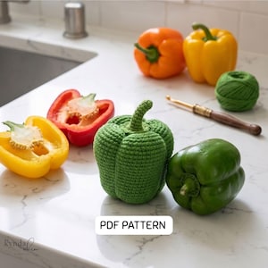 May include: A green crocheted bell pepper next to a real green bell pepper, with a yellow and red bell pepper cut in half. An orange and yellow bell pepper are in the background. A ball of green yarn and a crochet hook are also present. The text "PDF PATTERN" is visible.