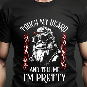 Puede incluir: Camiseta negra con un gorila con gafas de sol y gorra, con el texto "TOUCH MY BEARD AND TELL ME I'M PRETTY" en blanco. El diseño incluye detalles de llamas rojas. La camiseta es de cuello redondo.
