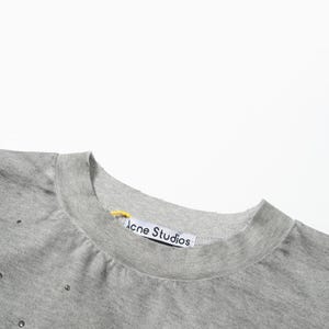 May include: A heather gray crew neck sweatshirt featuring small metallic studs scattered across the fabric. The interior collar displays a white brand label with the text Acne Studios in black, accompanied by a small yellow fabric loop.