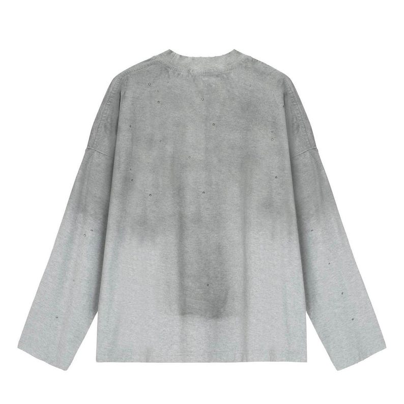 May include: A long-sleeve crew neck shirt in a light gray color featuring a subtle gradient effect that transitions to a darker gray tone toward the top. The garment displays a distressed aesthetic with small, scattered holes throughout the fabric.