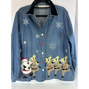 May include: A blue denim button-up shirt with a black velvet collar. The shirt is decorated with white snowflake appliqués and festive appliqués of Santa Claus and reindeer. The shirt has white buttons and one red button.