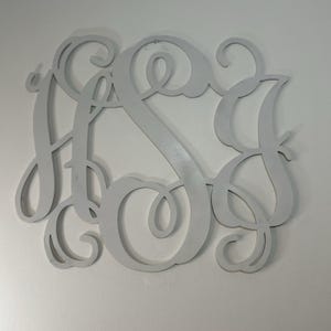 Peut inclure: Un monogramme en bois gris clair représentant les lettres entrelacées H, S et J. Les lettres sont dans une police cursive, avec des volutes et des courbes décoratives. Le monogramme est conçu pour être monté sur un mur.