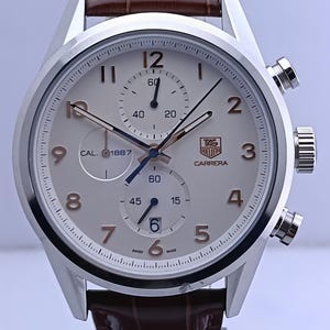 Op de afbeelding: Zilverkleurig Carrera horloge met een lichtgekleurde wijzerplaat, zwarte en gouden cijfers en wijzers. Het horloge heeft een bruine leren band en meerdere sub-wijzerplaten. De wijzerplaat toont de tekst "CARRERA" en "SWISS MADE".
