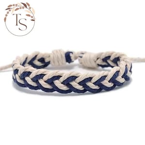 May include: Braided bracelet with a nautical theme. The bracelet is made from cream and navy blue rope, woven in a thick, textured pattern. The bracelet is displayed against a white background.