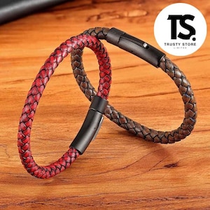 May include: Two braided leather bracelets. One is red, the other is brown. Both have black metal clasps. The bracelets are displayed on a wooden surface. The logo for Trusty Store is in the upper right corner.